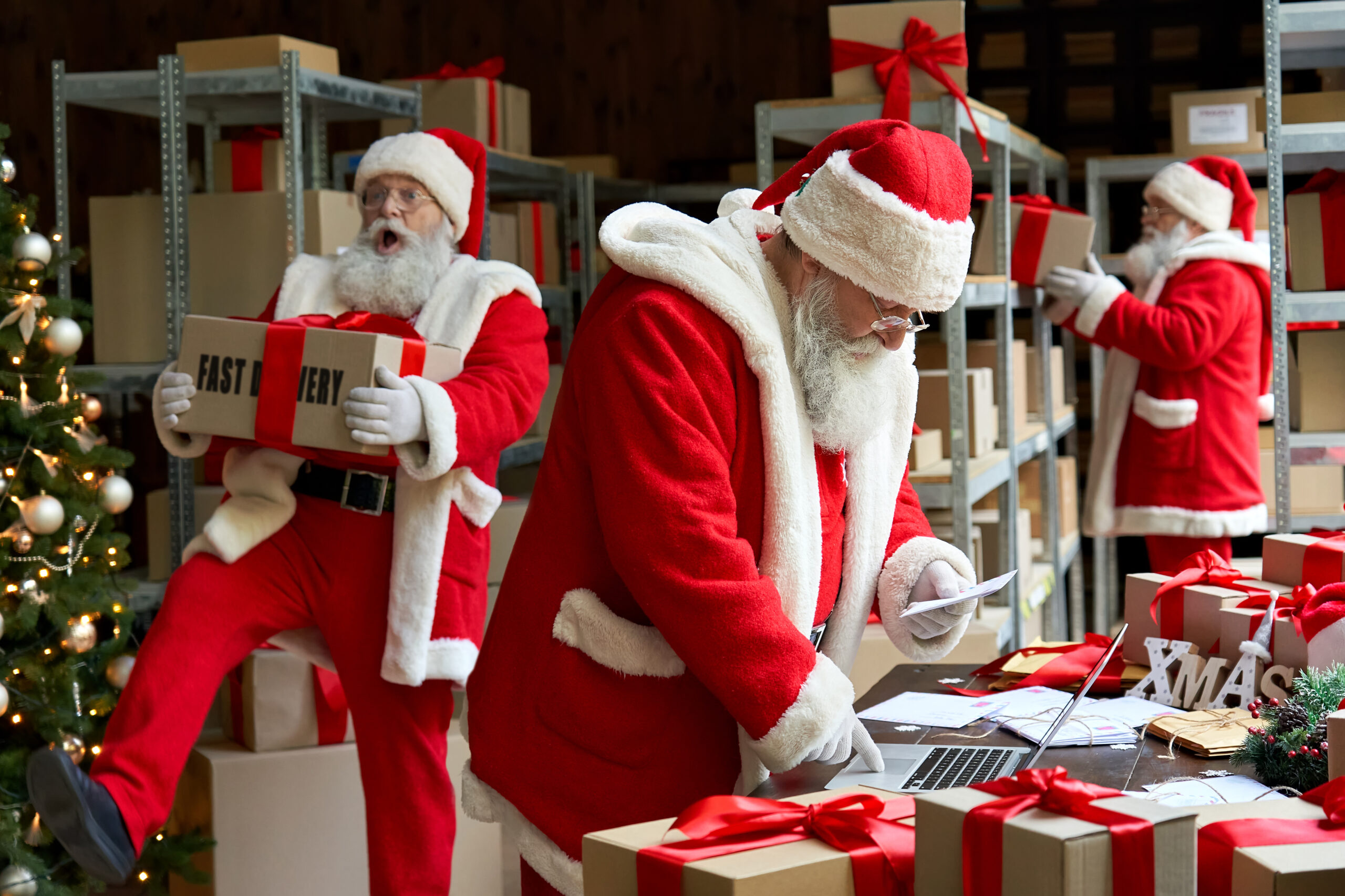 Many busy Santa Clauses packing gift boxes preparing fast xmas delivery. Three funny Santas walking in workshop warehouse in Merry Christmas rush delivering presents during holiday preparations.